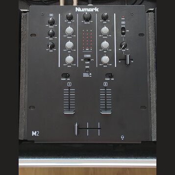 Černý DJ mixér značky Numark s označením M2 v levém dolním rohu. Přístroj obsahuje řadu otočných knoflíků pro ovládání GAIN, TREBLE, MID a BASS, cent…