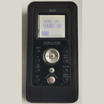 Černý přenosný digitální nahrávač značky KORG. Na displeji je text KORG SR1 SOUND ON a fialový sloupec indikátoru. Pod displejem je nápis SOUND on SO…