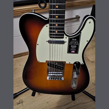 Elektrická kytara typu Telecaster s barevným přechodem korálovo-černé (sunburst) a krémovým pickguardem. Na pickguardu je černý štítek s nápisy „Fend…
