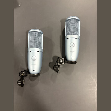 Dva stříbřité kondenzátorové mikrofony s mřížkou v horní části a černým držákem u základny. Na obou je viditelné logo AKG a nápis PERCEPTION 120. Mik…
