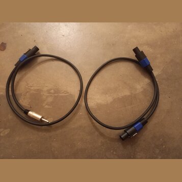 Dvě černé audio kabeláže s modrými plastovými konektory. Levý kabel má na jednom konci 6,3mm jack konektor a na druhém nečitelně označený vícepinový…