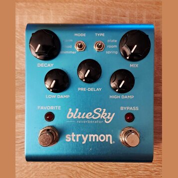 Modře anodizovaný efekt pedál s nápisy blueSky reverberator a strymon. Obsahuje pět černých otočných ovladačů s bílou značkou a dva přepínače typu to…