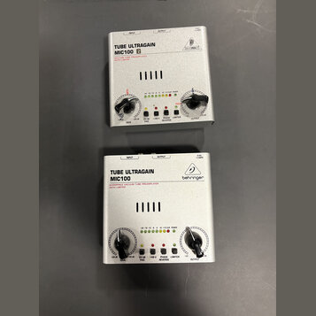 Dvě stříbrná zařízení s nápisem TUBE ULTRAGAIN MIC100. Horní jednotka má vedle modelu bílé čtverečky s čísly 1 a 2 a logo BEHRINGER v kruhu. Spodní j…