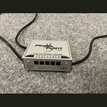 Stříbrný napájecí adaptér s nápisem POWER PLANT Junior. Na horní části je text 9 VOLT DC OUTPUTS - ISOLATED a číslování výstupů od 1 do 5. Přední pan…