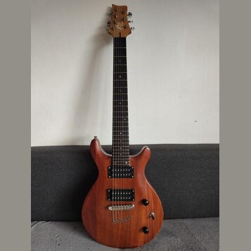 Elektrická kytara s hnědým dřevěným korpusem a tmavým hmatníkem. Na hlavě je viditelné logo "JD". Nástroj má dva černá humbuckery, jeden přepínač a d…