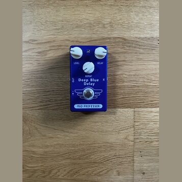 Modrý efekt pedál s bílými ovládacími knoflíky. Na přední straně jsou nápisy LEVEL, DELAY, REPEAT a uprostřed model Deep Blue Delay. Ve spodní části…