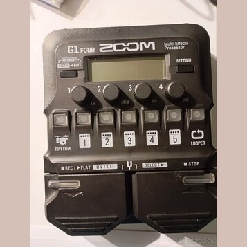 Černý multi-efektový procesor s nápisy G1 FOUR, ZOOM a Multi-Effects Processor. Zařízení má displej, čtyři otočné ovladače s popisky Lo, Mid, Hi a Vo…