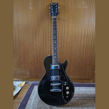 Černá elektrická kytara s tvarem single-cut a hnedým hmatníkem. Na hlavě je bílý nápis Emperor. Nástroj má dva humbuckery, stříbrný most a tři ovláda…