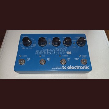 Modrý efekt pedál s nápisem FLASHBACK X4 a logem tc electronic. Na horní části jsou čtyři ovládací knoflíky s popisky TONEPRINT, TIME, FEEDBACK a DEL…