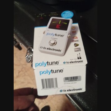 Bílý kytarový tuner v originální krabici. Na přístroji i na obalu jsou nápisy „polytune“ a „tc electronic“, dále je zde text „true bypass“. Displej t…