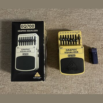 Žlutý kytarový pedál s černým spodním panelem, na kterém je logo behringer. Na horní části jsou nápisy GRAPHIC EQUALIZER a EQ700, vstupy OUT a IN a ř…