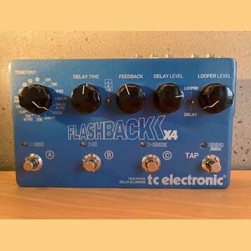 Modrý efekt pedál s nápisem FLASHBACK X4 a logem tc electronic. Zařízení má čtyři černé ovládací knoflíky s popisky TONEPRINT, DELAY TIME, FEEDBACK,…