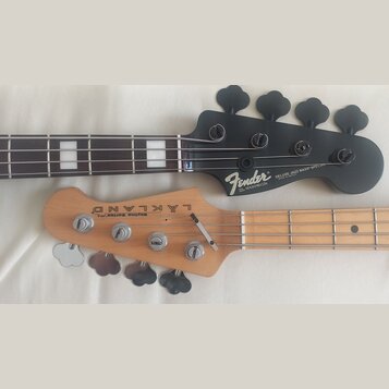 Fotografie zachycuje hlavy dvou basových kytar. Horní je černá s nápisy Fender, DELUXE JAZZ BASS SPECIAL, MADE IN MEXICO a sériovým číslem MXD1901226…