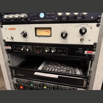 Fotografie zachycuje několik kusů rackového studiového vybavení v šedém racku. Horní jednotka je bílá s nápisy WARM AUDIO a WA-2A LEVELING AMPLIFIER,…