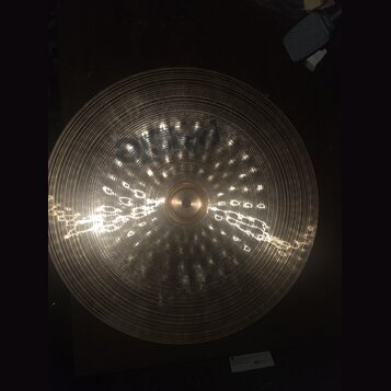 Kruhový mosazný činel s koncentrickými drážkami na povrchu. Na horní části je viditelný tmavý nápis PAISTE. Povrch vykazuje odrazy světla a drobné ne…