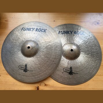 Dvě kovové činely s kovaným povrchem v přirozené barvě. Oba mají nápis FUNKY ROCK a logo s nečitelným textem v dolní části. Na horním činele je drobn…