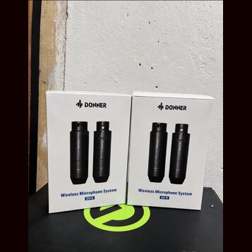 Dvě bílé krabice s nápisem DONNER a označením Wireless Microphone System CV-2. Na krabicích jsou vyobrazeny dva černé bezdrátové mikrofony. Krabice s…