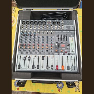 Stříbrný mixážní pult značky behringer, model XENYX X1222USB. Zařízení je umístěno v ochranném černém kufru s pěnovou výplní. Na panelu jsou vidět po…