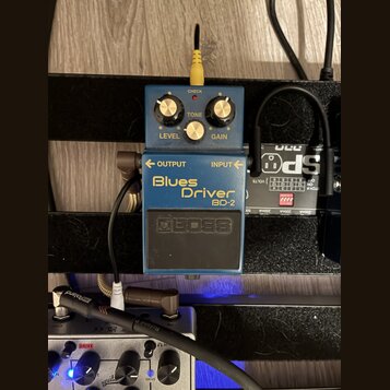 Modrý efekt pedál s nápisy Blues Driver a BD-2. Na spodní části je viditelné logo BOSS. Pedál má tři ovládací knoflíky s popisky LEVEL, TONE a GAIN a…