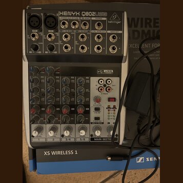 Stříbrný mixážní pult značky behringer s označením XENYX Q802USB. Zařízení obsahuje čtyři vstupní kanály s ovládacími prvky pro GAIN, EQ a LEVEL, USB…