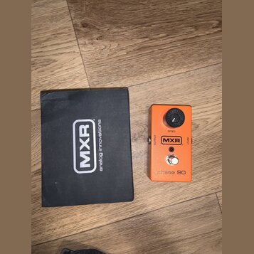 Oranžový kytarový efekt s černým ovládacím knoflíkem a nápisy SPEED, OUTPUT, INPUT a MXR. Ve spodní části je vyražen text phase 90. Vedle efektu leží…