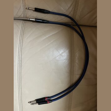 Dvě modré audio kabeláže s konektory typu jack. Na jednom konci jsou oba konektory stříbrné, na druhém konci mají černé kryty s červenými prstenci. N…
