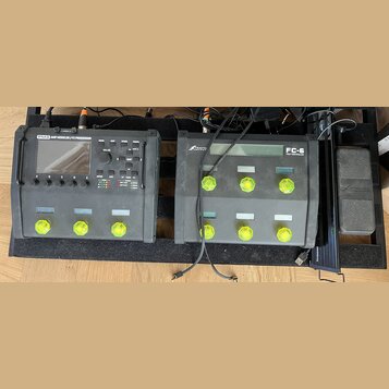 Na černém pedalboardu jsou umístěna dvě zařízení značky Fractal Audio Systems. Vlevo je procesor s nápisem FM3 AMP MODELER / FX PROCESSOR, vpravo je…