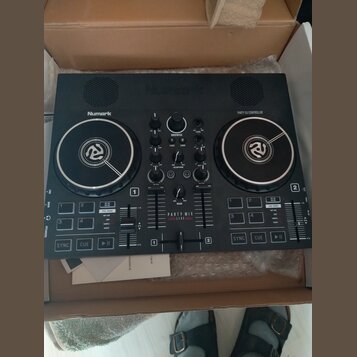Černý DJ kontrolér značky Numark s nápisem PARTY DJ CONTROLLER. Uprostřed je uveden model PARTY MIX LIVE. Zařízení obsahuje dva jog-wheels, několik p…
