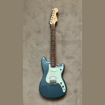 Modře lakovaná elektrická kytara s bílým pickguardem a hnedým hmatníkem. Na hlavě krku je viditelné logo Fender. Nástroj má tři snímače, pětiknobové…