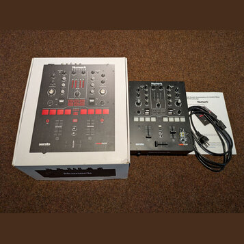 Fotografie zobrazuje černý DJ mixér, jeho originální krabici s obrázkem produktu a přibalený napájecí kabel s dokumentací. Na přístroji i na krabici…