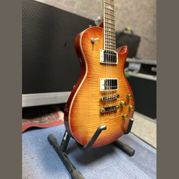 Elektrická kytara s trupem v barvě sunburst a viditnou strukturou dřeva. Nástroj má dva humbuckery s bílými rámečky, čtyři zlaté ovládací knofíky a z…