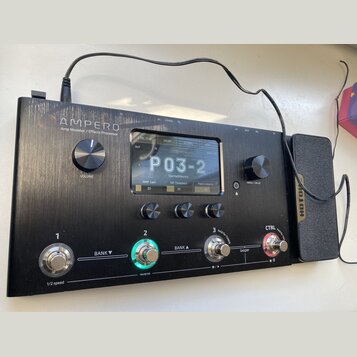 Černý efektový procesor s nápisem AMPERO Amp Modeler / Effects Processor. Zařízení má digitální displej, na kterém je zobrazen text P03-2 a další par…