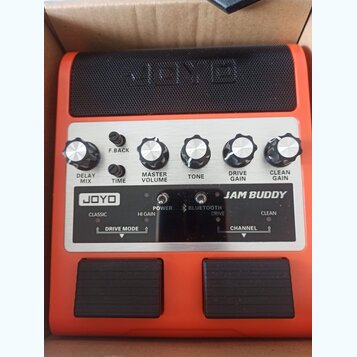 Oranžový kytarový kombo zesilovač s černým reproduktorem. Na ovládacím panelu jsou knoflíky s popisky DELAY MIX, F.BACK, TIME, MASTER VOLUME, TONE, D…
