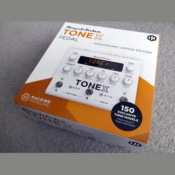 Fotografie znázorňuje bílou krabici s produktem AmpliTube TONEX PEDAL ANNIVERSARY LIMITED EDITION. Na krabici je zobrazen bílý efekt pedál s displeje…
