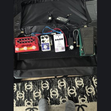 V černé přepravní tašce je umístěno několik efektových pedálů propojených kabely. Zleva jsou vidět červený pedal s nápisem "Electro-Harmonix" a "Sava…