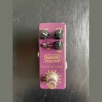 Fialový kytarový efekt s třemi černými otočnými knoflíky popsanými jako VOLUME, DRIVE a TONE. Na přední straně je malý přepínač s nápisy OD, BOOST a…
