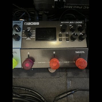 Šedý efektový pedál s nápisy BOSS a REVERB RV-500. Zařízení má displej, několik otočných potenciometrů a ovládací tlačítka s nápisy WRITE, EXIT a EDI…