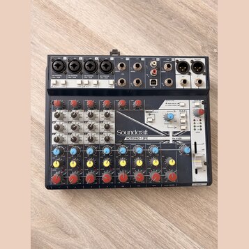 Černý mixážní pult s bílými a šedými popisky. Na předním panelu je vidět značka Soundcraft a název modelu NOTEPAD-12FX, dále nápis Lexicon EFFECTS a…