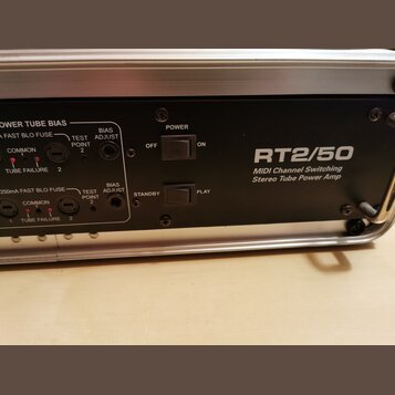 Detail zadní strany černého zesilovače s nápisem RT2/50 a popiskem MIDI Channel Switching Stereo Tube Power Amp. Jsou zde vidět dva přepínače s označ…