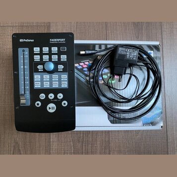 Černý kontrolér PreSonus FADERPORT Production Controller s řadou tlačítek a posuvníkem na levé straně. Vedle zařízení je položen jeho původní kartono…