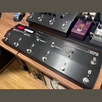 Černý efektový spínací systém s nápisem BOSS ES-8 EFFECTS SWITCHING SYSTEM. Zařízení má osm kovových spínacích tlačítek, z nichž šest je očísleno čís…