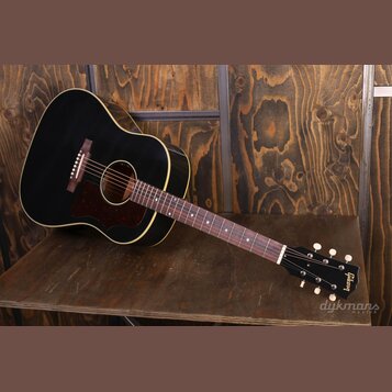 Černá akustická kytara s hnědým rýhovaným plechtrem a bílým lemováním korpusu. Na hlavě nástroje je zlatý nápis Gibson. Hриф má tmavou hmatovnici s j…