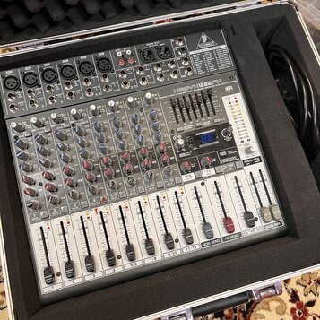 Stříbrný mixážní pult v přepravním kufru s černé pěnou. Na horní části je nápis BEHRINGER a modelové označení XENYX 1222FX. Zařízení obsahuje několik…