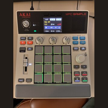 Bílá MPC Sample od značky AKAI professional. Zařízení má digitální displej, několik ovládacích knoflíků a 16 podsvícených padů s popisy funkcí. Na po…