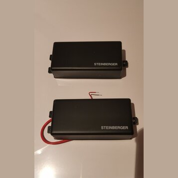 Dvě černé obdélníkové krabičky s nápisem STEINBERGER. Spodní kus má připojený červený kabel. Povrch je matný a v dobrém stavu.
