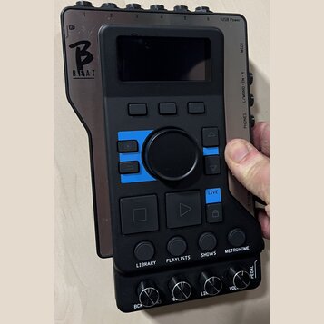 Černý elektronický přístroj s displejem a ovládacími prvky. Na levé straně je bílé logo s písmenem B a nápisem BEAT. Na spodní části jsou tlačítka s…