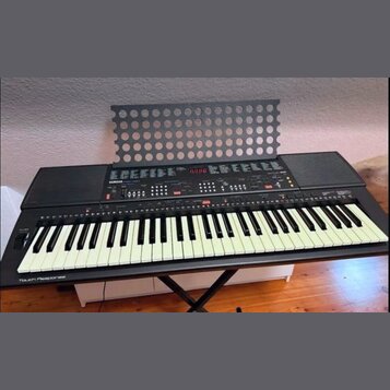 Černý digitální klavír s bílými klávesami, umístěný na černém X-stojanu. Na ovládacím panelu je nápis YAMAHA a vlevo dole u kláves nápis Touch Respon…