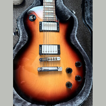 Elektrická kytara s tmelem v odstínu sunburst, umístěná v otevřeném pouzdře s šedým polstrováním. Nástroj má dva humbuckery s bílými kryty, chromovan…