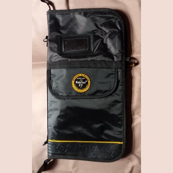 Černý textilní obal na hudební nástroj s žlutým pruhem v dolní části. Uprostřed je kulatý žlutý štít s nápisy ROCKBAG by Warwick, proudly made with R…