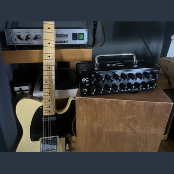 Na fotografii je elektrická kytara typu Telecaster v krémové barvě s černým pickguardem a javorovým hmatníkem. Vedle ní stojí černý kompaktní zesilov…